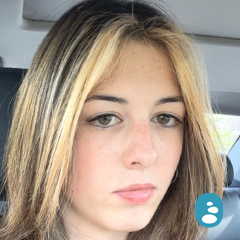 A person with light brown and blonde hair sits in a car, looking at the camera with a neutral expression. - OYESPA Aveda Lifestyle | nver Grove Heights, MN