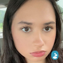 Close-up of a person with long, salon-styled dark hair and a serious expression, sitting in a car. - OYESPA Aveda Lifestyle | nver Grove Heights, MN