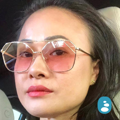 A beautiful woman with long dark hair and radiant skin, wearing large, angular sunglasses with pink-tinted lenses, sits in a car. - OYESPA Aveda Lifestyle | nver Grove Heights, MN