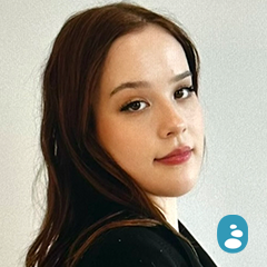 A young woman with long brown hair looks over her shoulder at the camera against a plain light background. An icon of a person is in the lower right corner. - OYESPA Aveda Lifestyle | nver Grove Heights, MN
